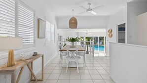 A bright, spacious hallway with white walls and a tiled floor leading to a dining area with a pool view. - Fairways Beach House - Stylish Beach House, Pet Friendly, Pool, Walk to Cafes, Beach (Sawtell)
