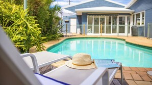 A poolside view with a lounge chair, a straw hat, and a book. - Fairways Beach House - Stylish Beach House, Pet Friendly, Pool, Walk to Cafes, Beach (Sawtell)