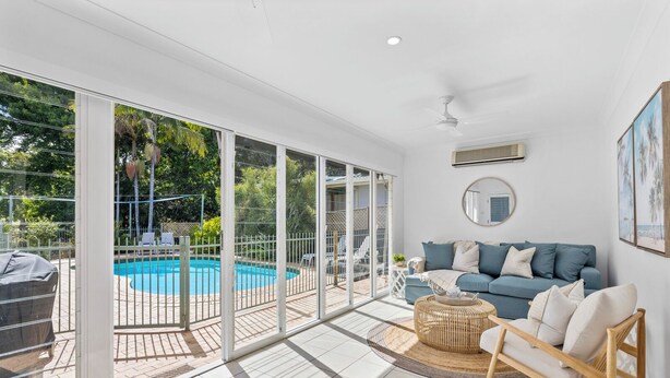 A spacious living area with a large sliding glass door leading to a pool, a blue sofa, and a wicker coffee table. - Fairways Beach House - Stylish Beach House, Pet Friendly, Pool, Walk to Cafes, Beach (Sawtell)
