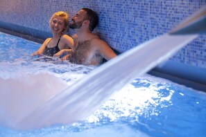 Un couple dans un jacuzzi, avec un mur carrelé en arrière-plan.