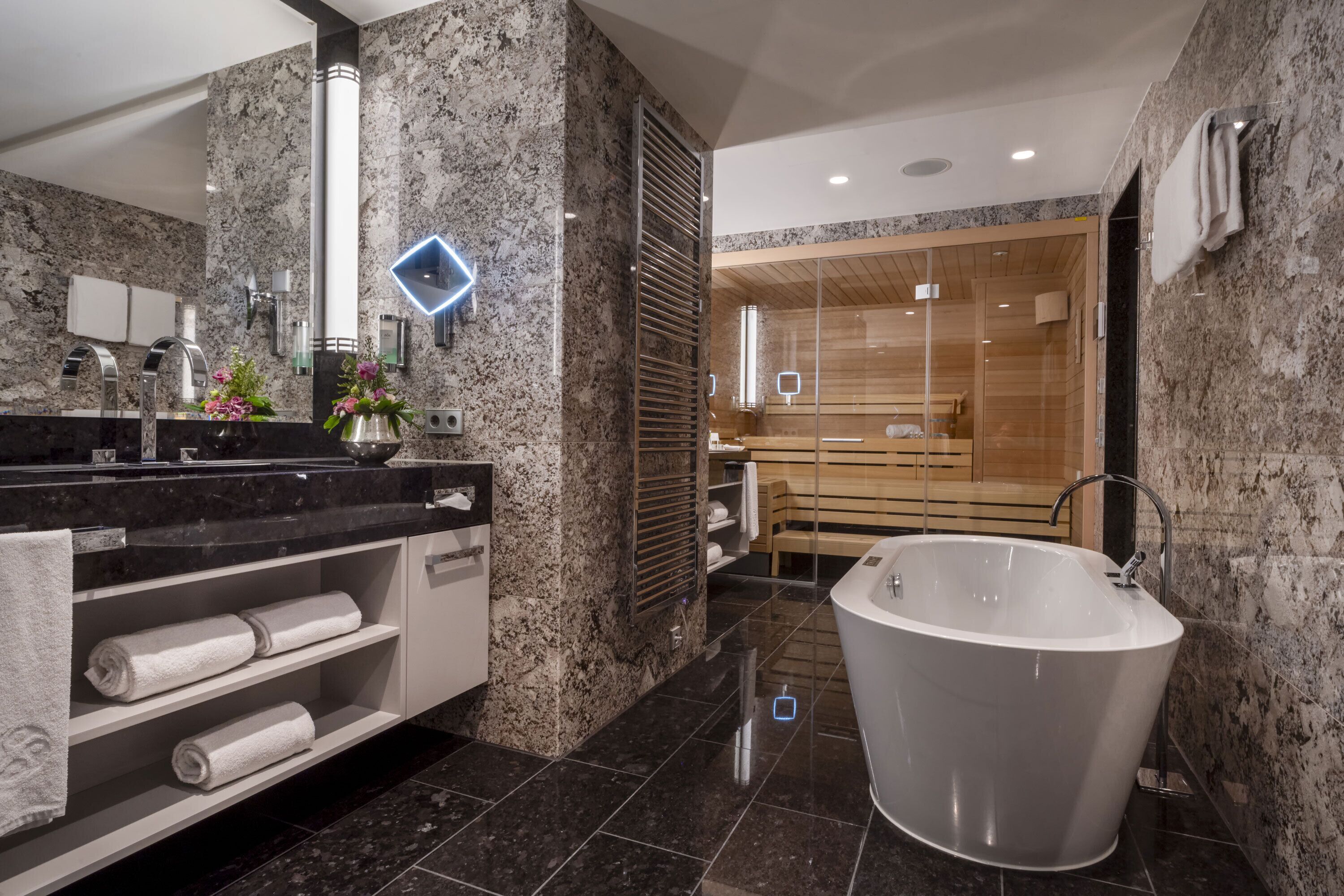 Ein modernes Badezimmer mit freistehender Badewanne, Granitwaschtischen und einem großen Spiegel.