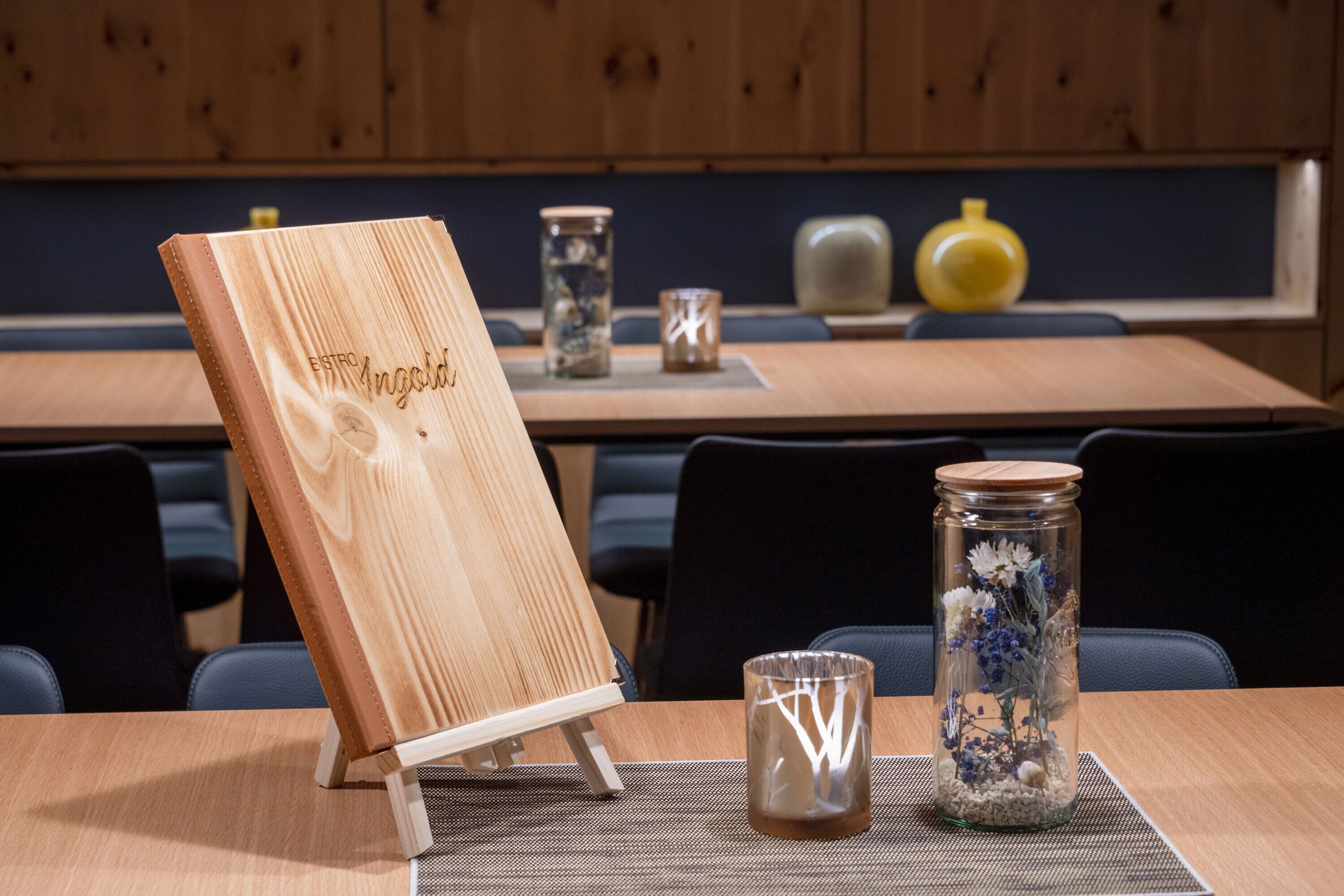 A wooden easel with a nameplate, a glass vase with flowers, and a small candle on a table.