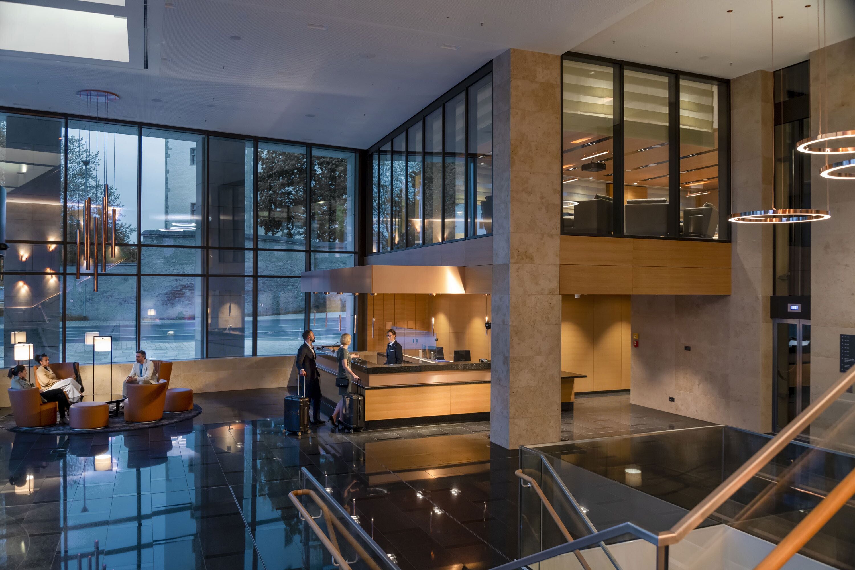 A spacious lobby with a reception desk, seating area, and a glass elevator.