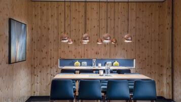 Ein moderner Essbereich mit einer Holzwand, einem langen Tisch, blauen Stühlen, hängenden Pendelleuchten und einem gerahmten Bild an der Wand.