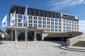 Un hôtel moderne à la façade sobre, doté de grandes fenêtres et d’une entrée imposante.