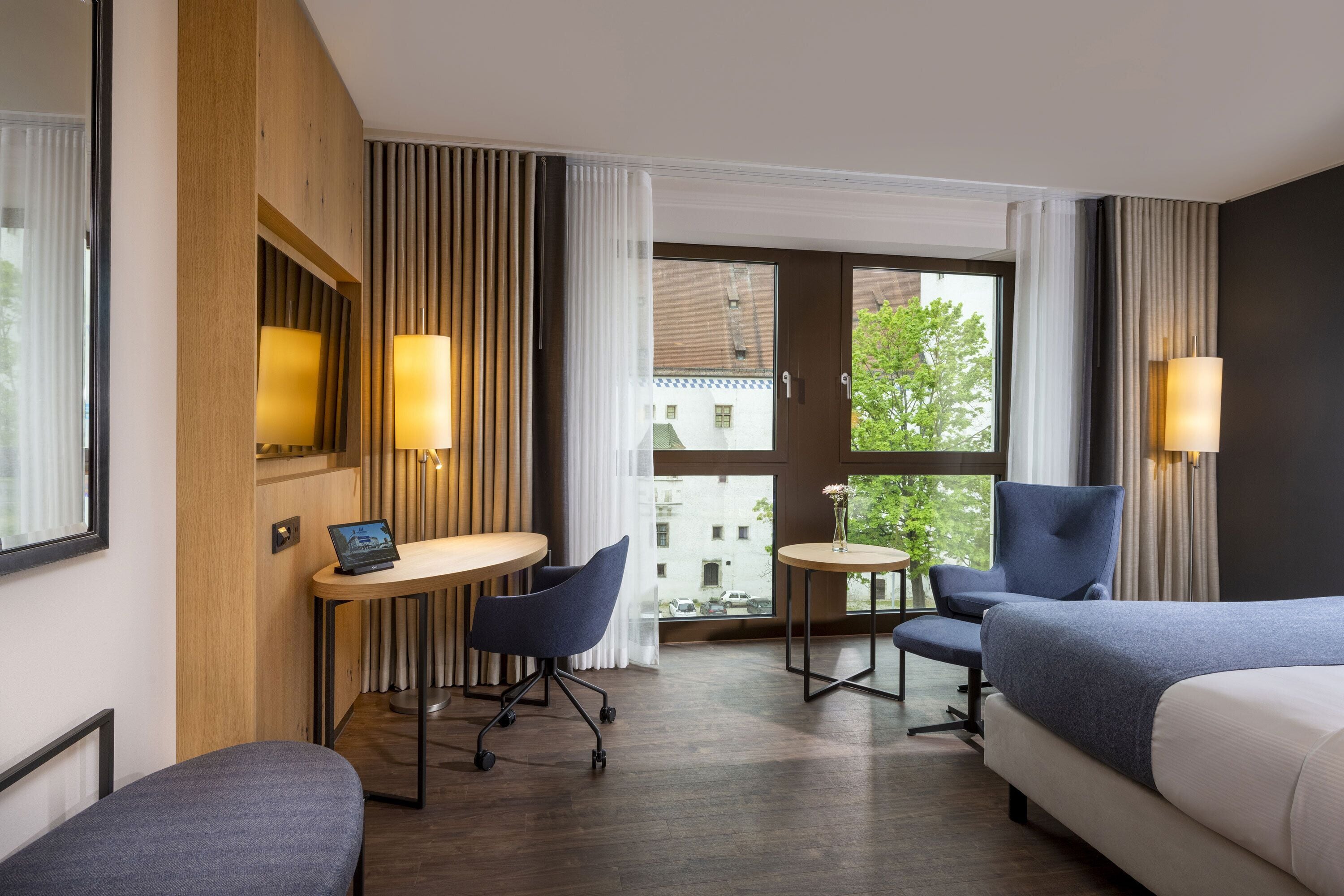 A hotel room with a bed, two armchairs, a small table, and a desk with a laptop.