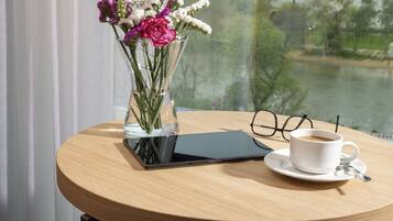 Ein runder Holztisch mit einem Tablet, einer Kaffeetasse, einem Brillenpaar und einer Blumenvase.