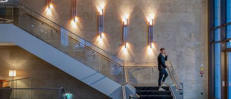 Un interior moderno con una escalera de cristal, barandillas metálicas e iluminación empotrada en la pared.
