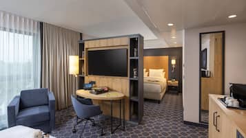 A hotel room with a bed, a desk with a computer, a chair, a small table, and a TV.