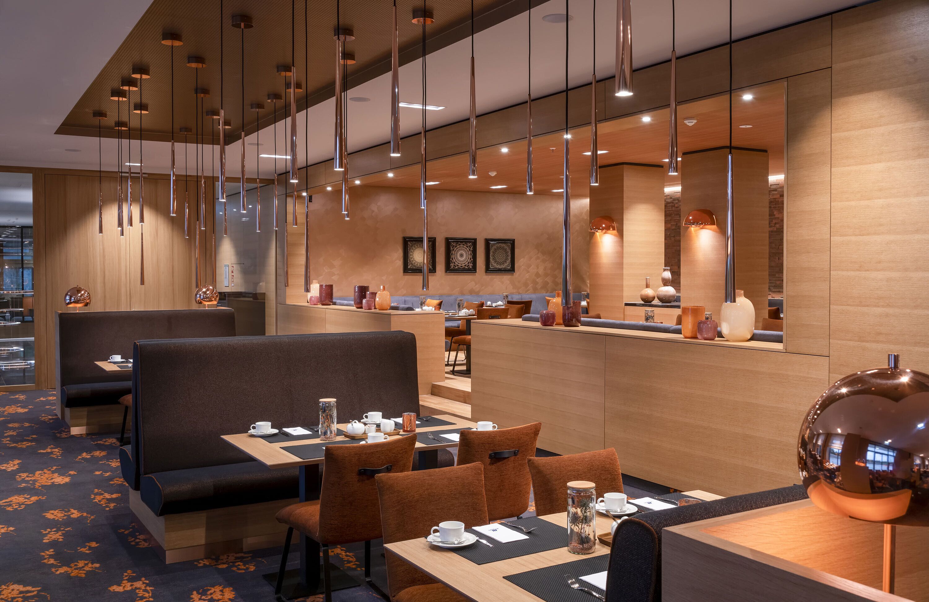 Un restaurant moderne avec des banquettes et des tables, des luminaires suspendus et un décor intérieur en bois.