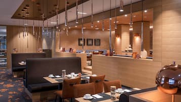 Ein modernes Restaurant mit Sitzecken und Tischen, schwebenden Pendelleuchten und einer Holzvertäfelung.