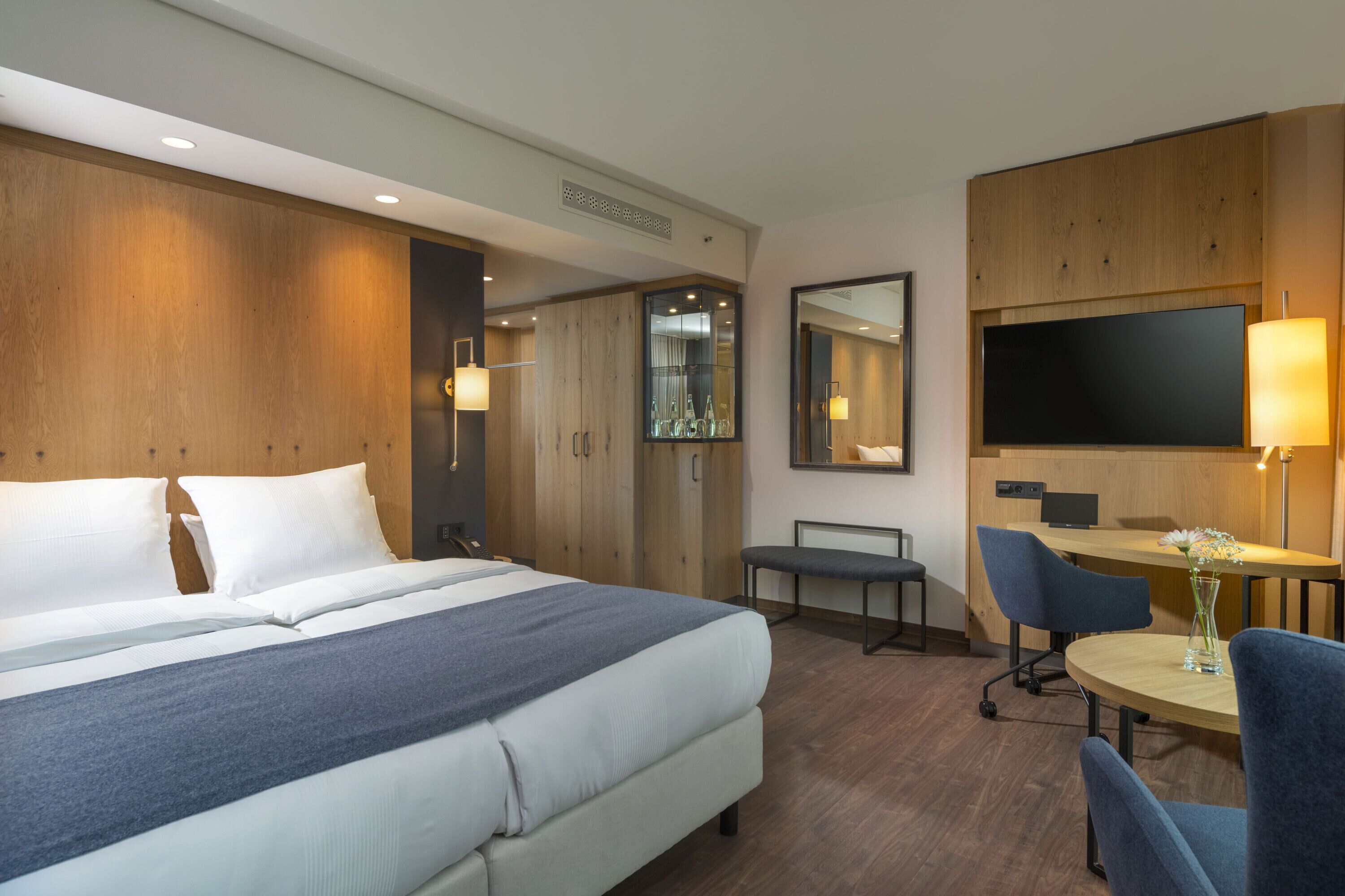 A hotel room with a bed, a desk, a chair, and a TV.