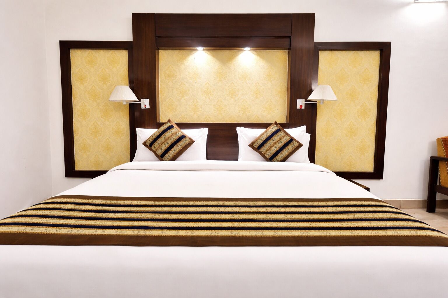A hotel room with a large bed, two bedside lamps, and a decorative headboard.