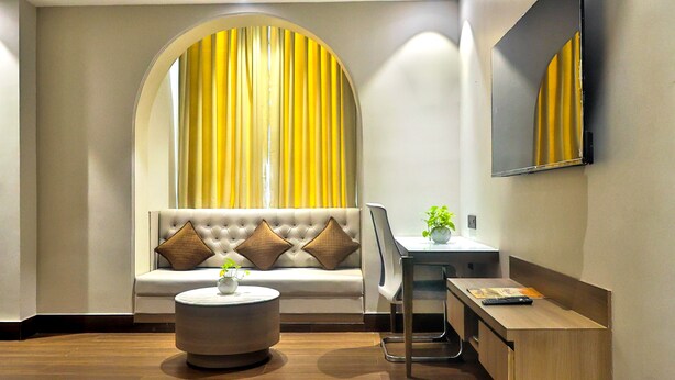 A modern living room with a sofa, a round coffee table, a desk with a chair, and a large mirror on the wall. - Hotel Kant Palace (Agra)