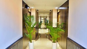 A hotel hallway with wooden paneling, potted plants, and a polished floor. - Hotel Kant Palace (Agra)