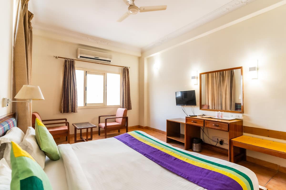 A hotel room with a bed, a desk, a chair, a television, and a window with curtains.