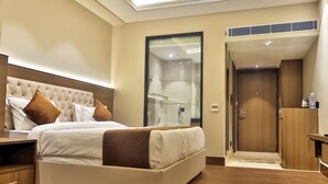 A modern hotel room with a large bed, a wooden headboard, a walk-in closet, and a bathroom with a glass shower enclosure. - Hotel Kant Palace (Agra)