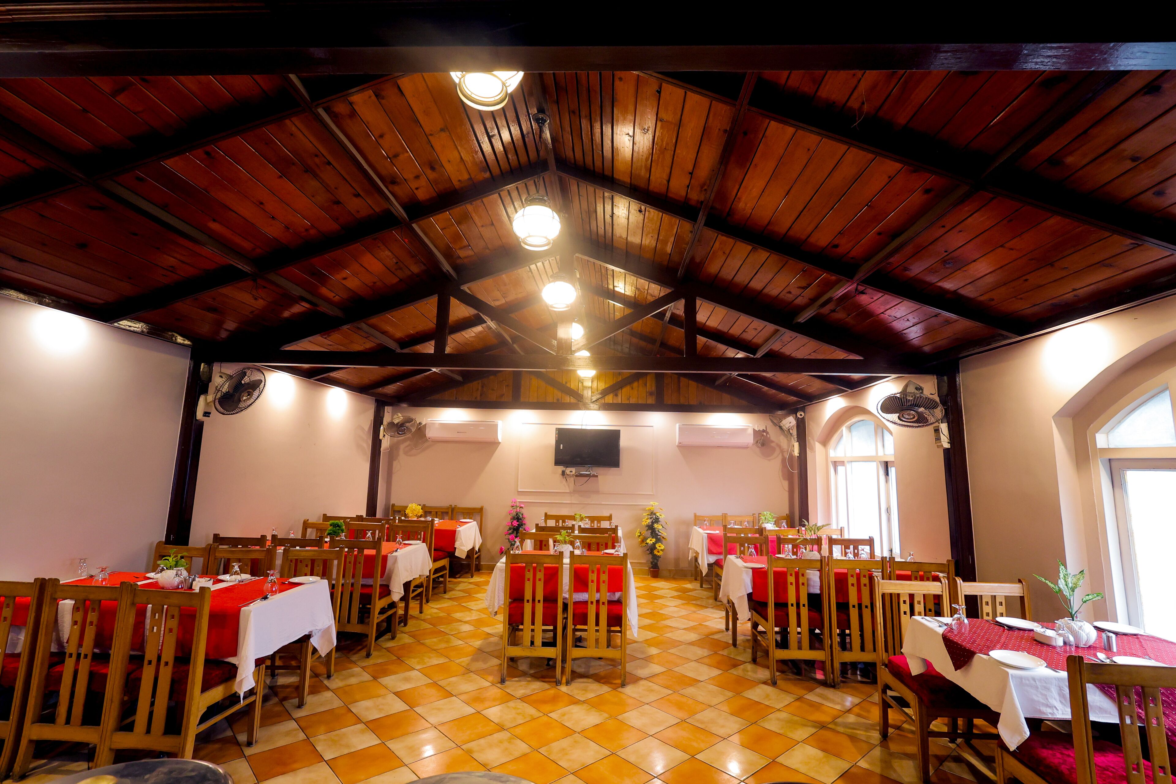 Un espace repas avec des tables et des chaises en bois, un sol carrelé et un haut plafond en bois agrémenté de luminaires.