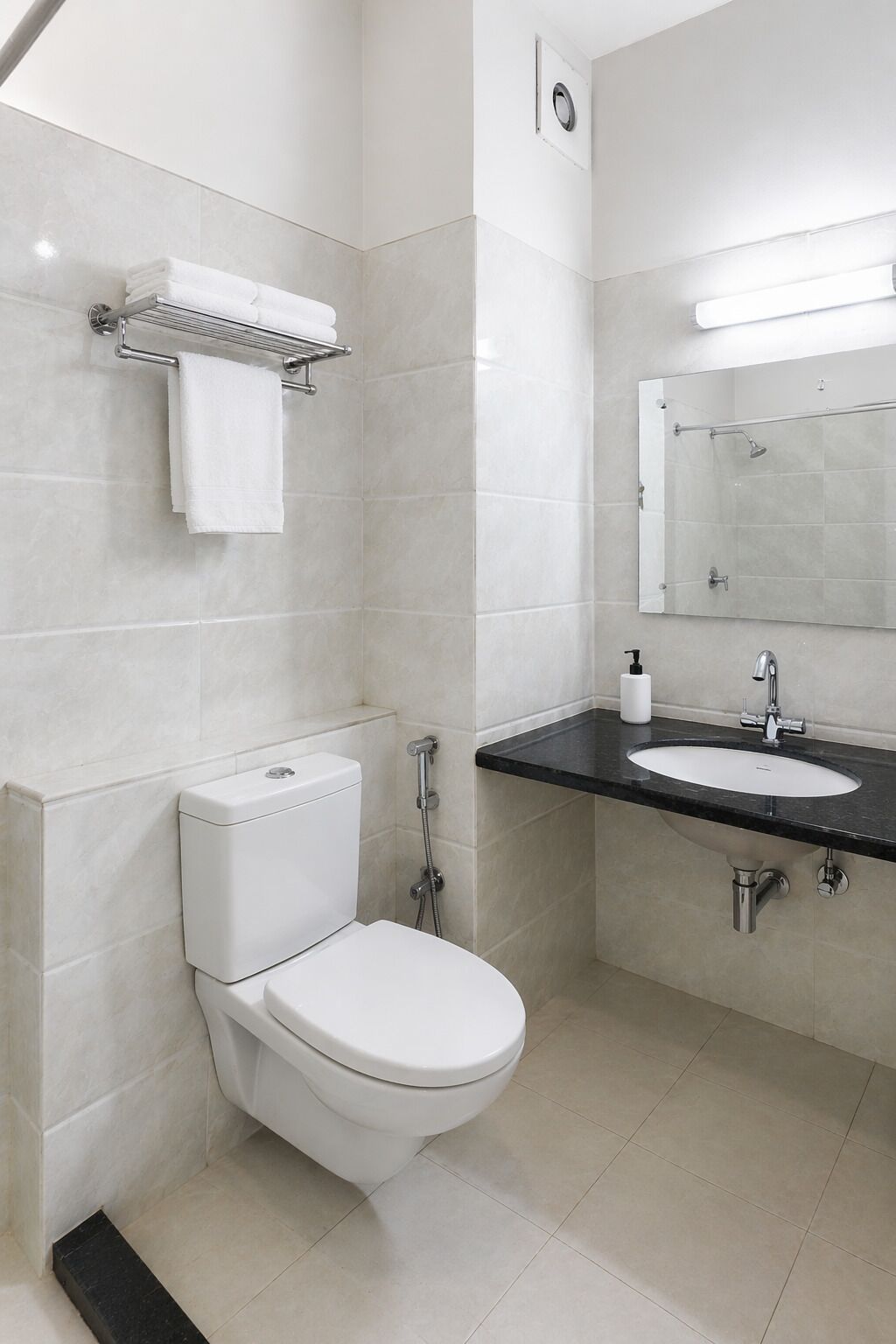 A modern bathroom with a white toilet, a sink with a black countertop, and a mirror above the sink.