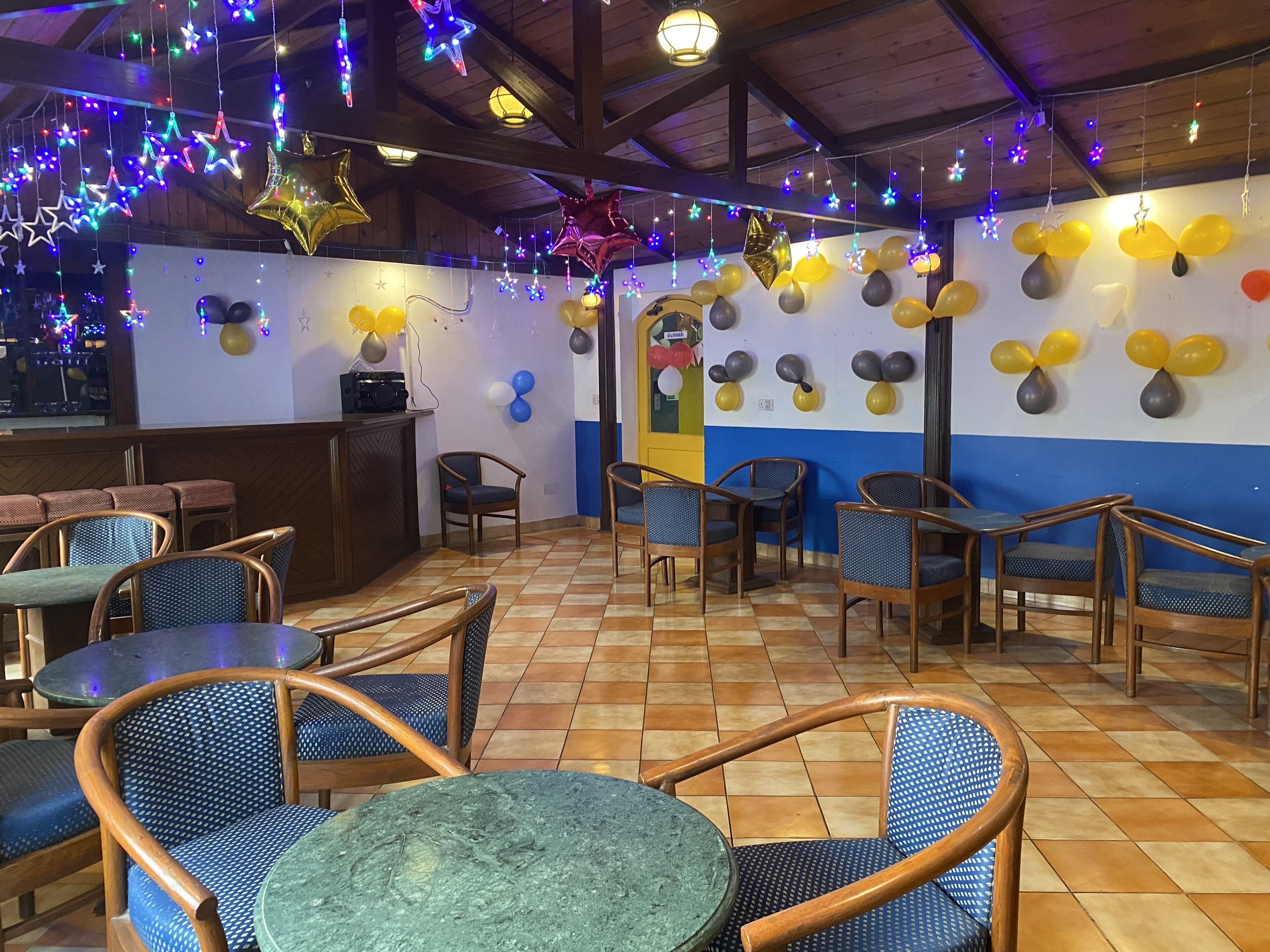 A restaurant with a tiled floor, wooden chairs, tables, and colorful star-shaped lights hanging from the ceiling.