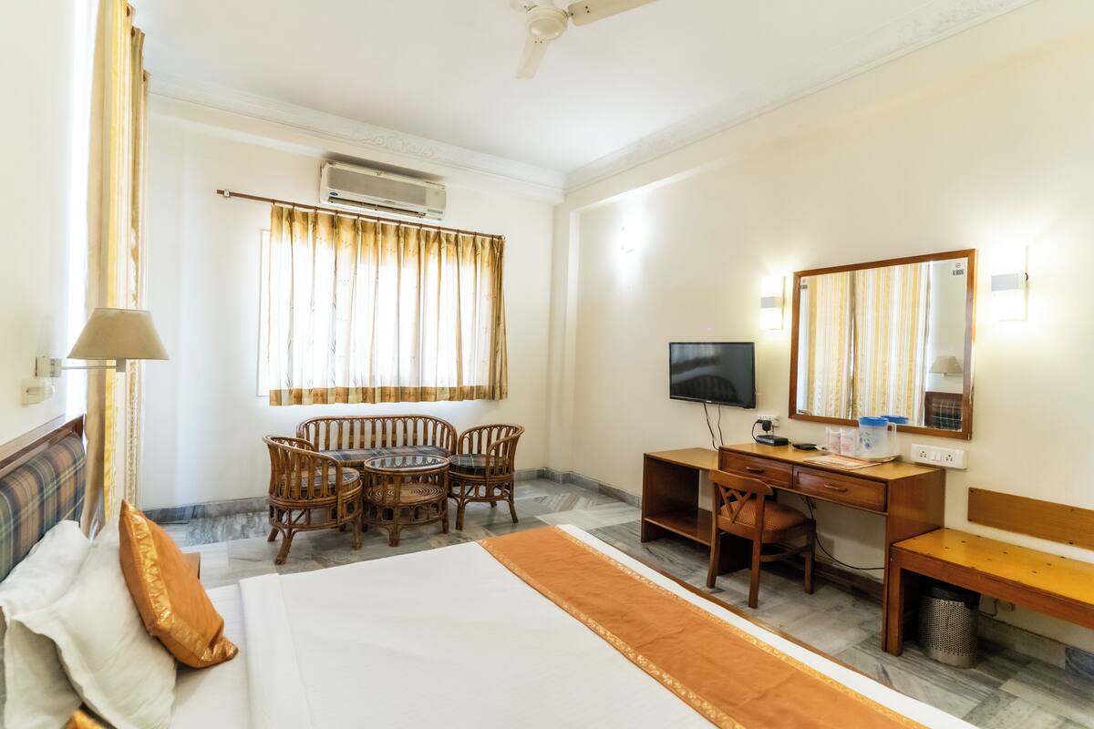 A hotel room with a bed, desk, chair, TV, and air conditioning unit.