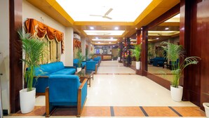 A hotel lobby with blue sofas, potted plants, and a reception desk. - Hotel Kant Palace (Agra)