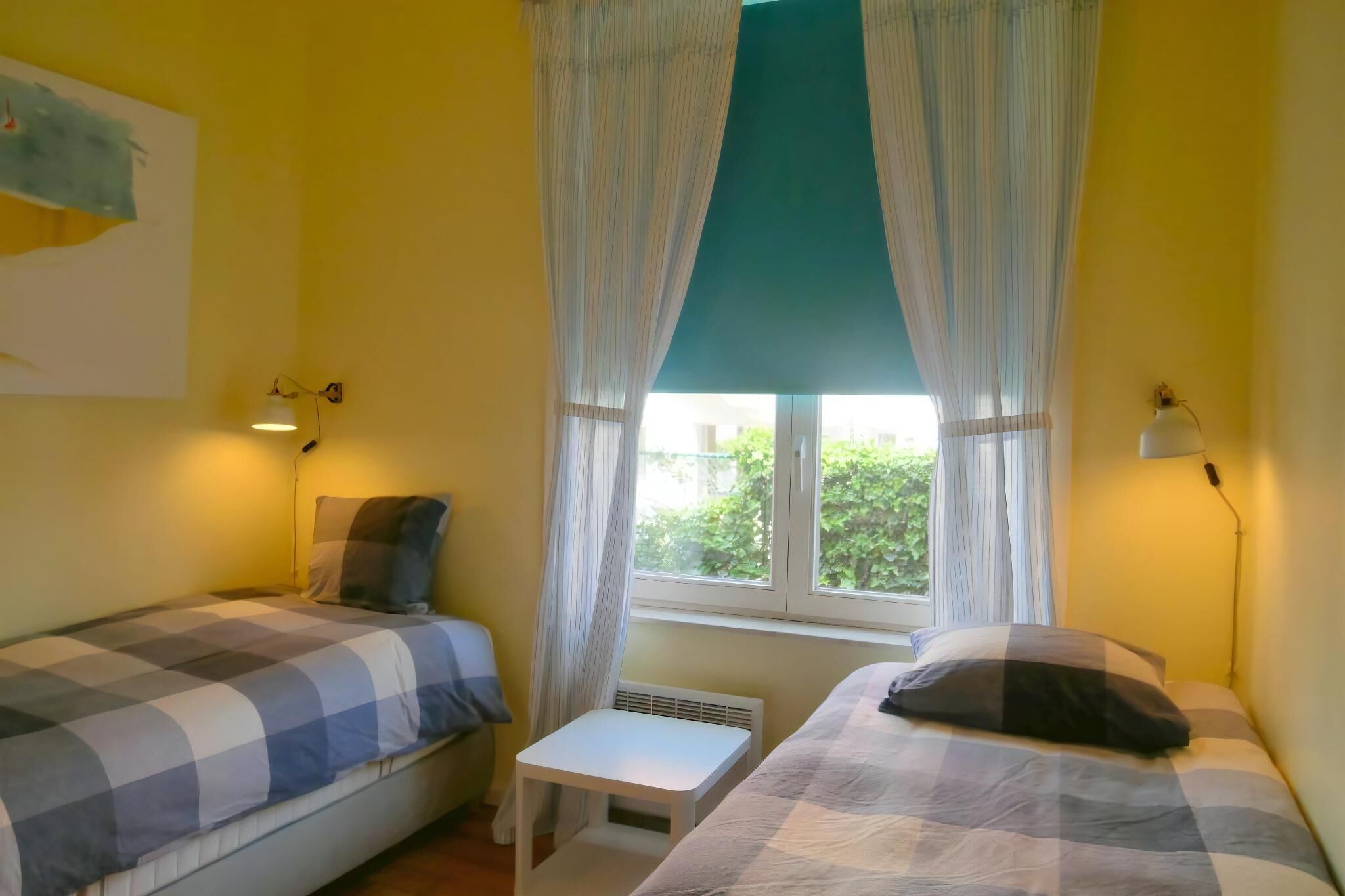A room with two beds, a small table, and a window with curtains.