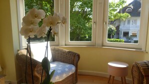 A wicker sofa with a star-patterned cushion, a small round stool, and a potted orchid plant.