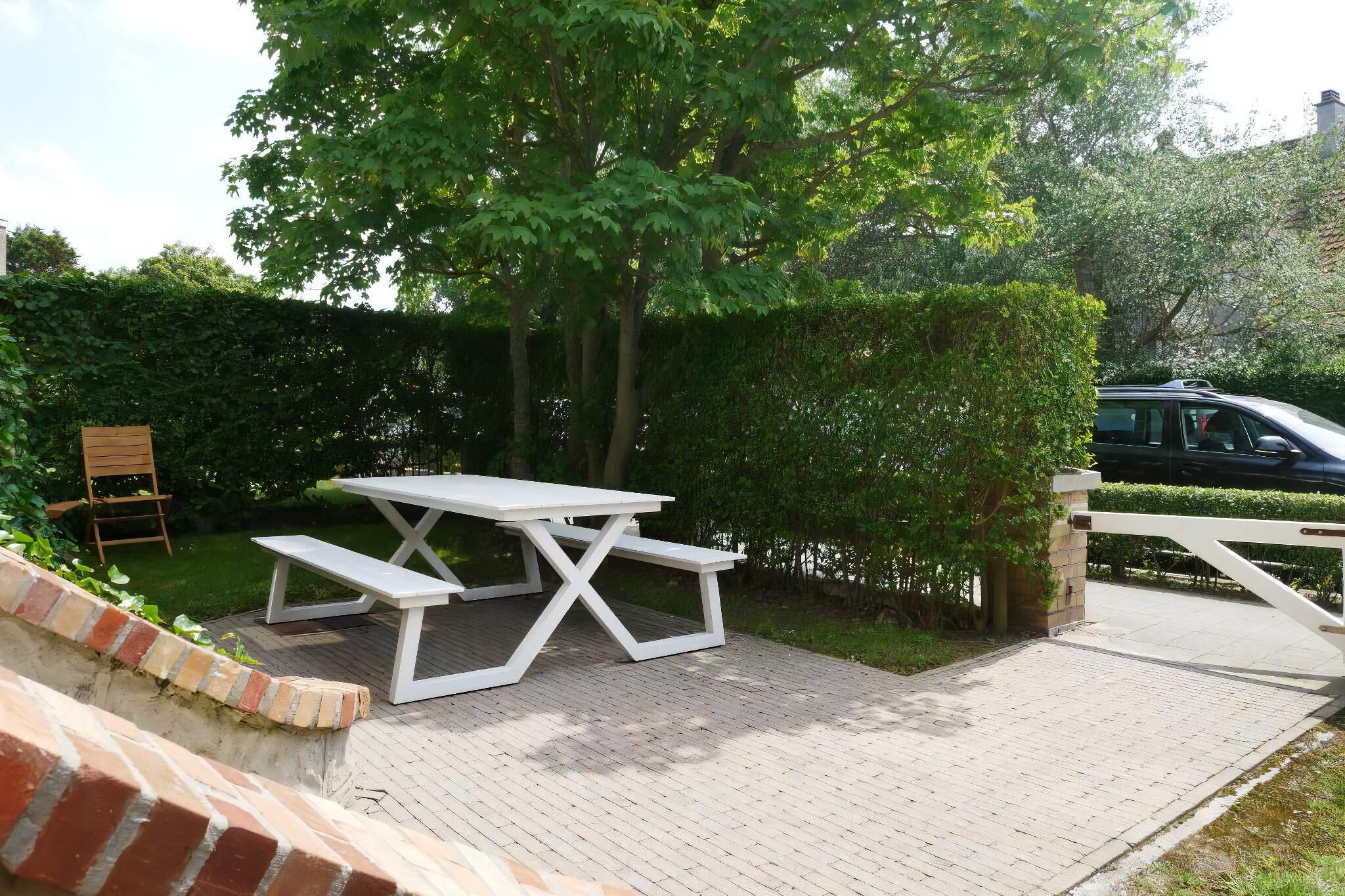Ein Picknicktisch mit Bänken, umgeben von Grünpflanzen und einem Pflasterweg.