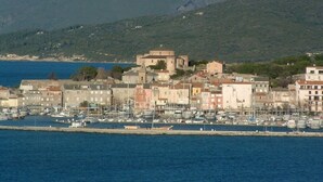Un pueblo costero con un puerto deportivo, edificios históricos y montañas al fondo.
