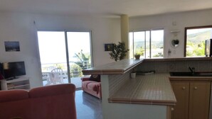 Una cocina moderna con una isla central, un área de comedor con un sofá rosa y un televisor en la sala.