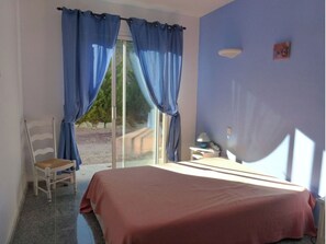 Cozy retreat with a large bed, chair, and table, set against a window with blue curtains.