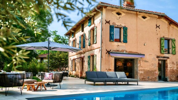 A two-story building with a pool, outdoor seating, and a large umbrella.