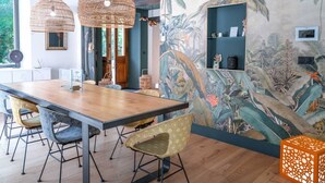 A dining area with a wooden table and chairs, woven pendant lights, and a tropical mural on the wall.