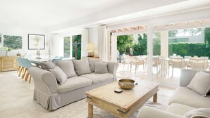 Een ruime woonkamer met een beige bank, een houten salontafel en een eethoek met witte stoelen.