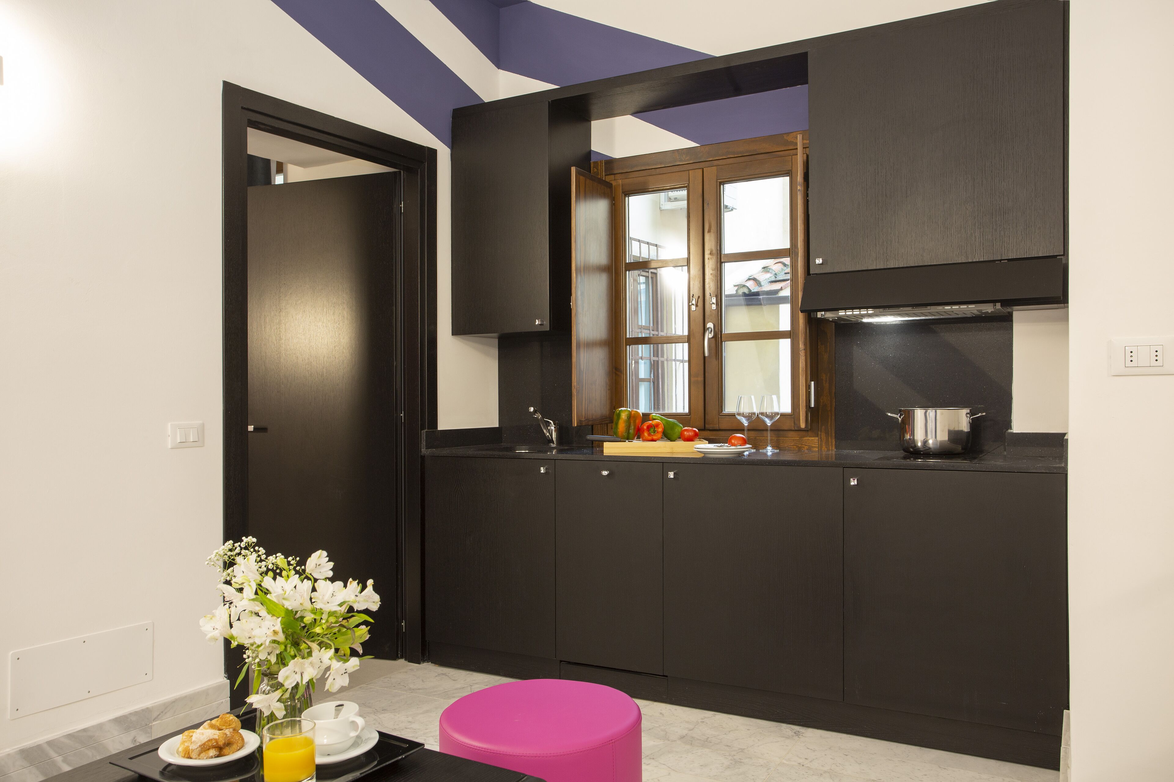 A modern kitchen with dark cabinetry, a window, and a pink stool.