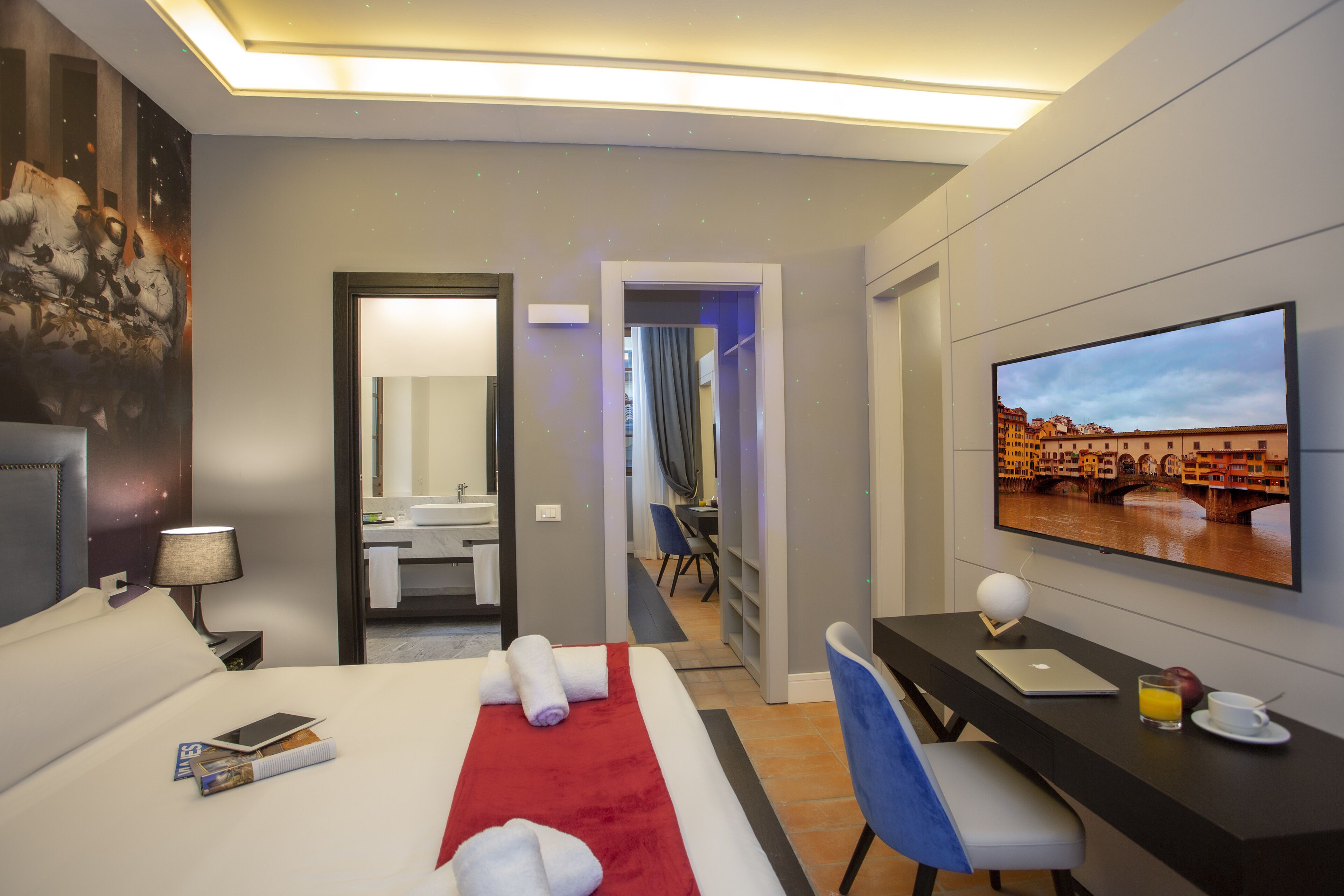 A hotel room with a bed, a desk, a TV, and a bathroom visible through an open door.