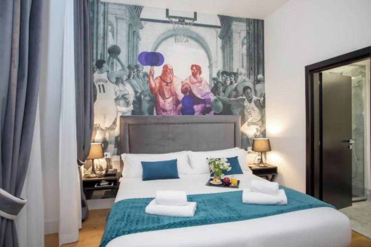 A hotel room with a large bed, two bedside tables with lamps, a headboard, and a mural on the wall.