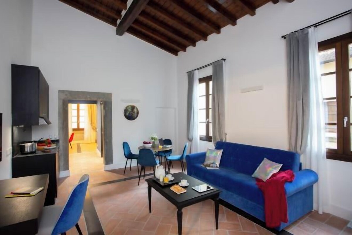 A living room with a blue sofa, a coffee table, and a dining area with chairs and a table.