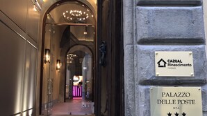 L’entrée d’un hôtel, avec un lustre, un comptoir d’accueil et des panneaux indiquant « CAZUAL RINASCIMENTO FIRENZE » et « PALAZZO DELLE POSTE ».