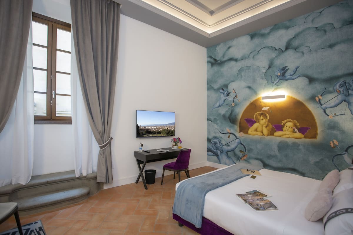 Un dormitorio con cama, escritorio, silla, ventana con cortinas y un mural en la pared.