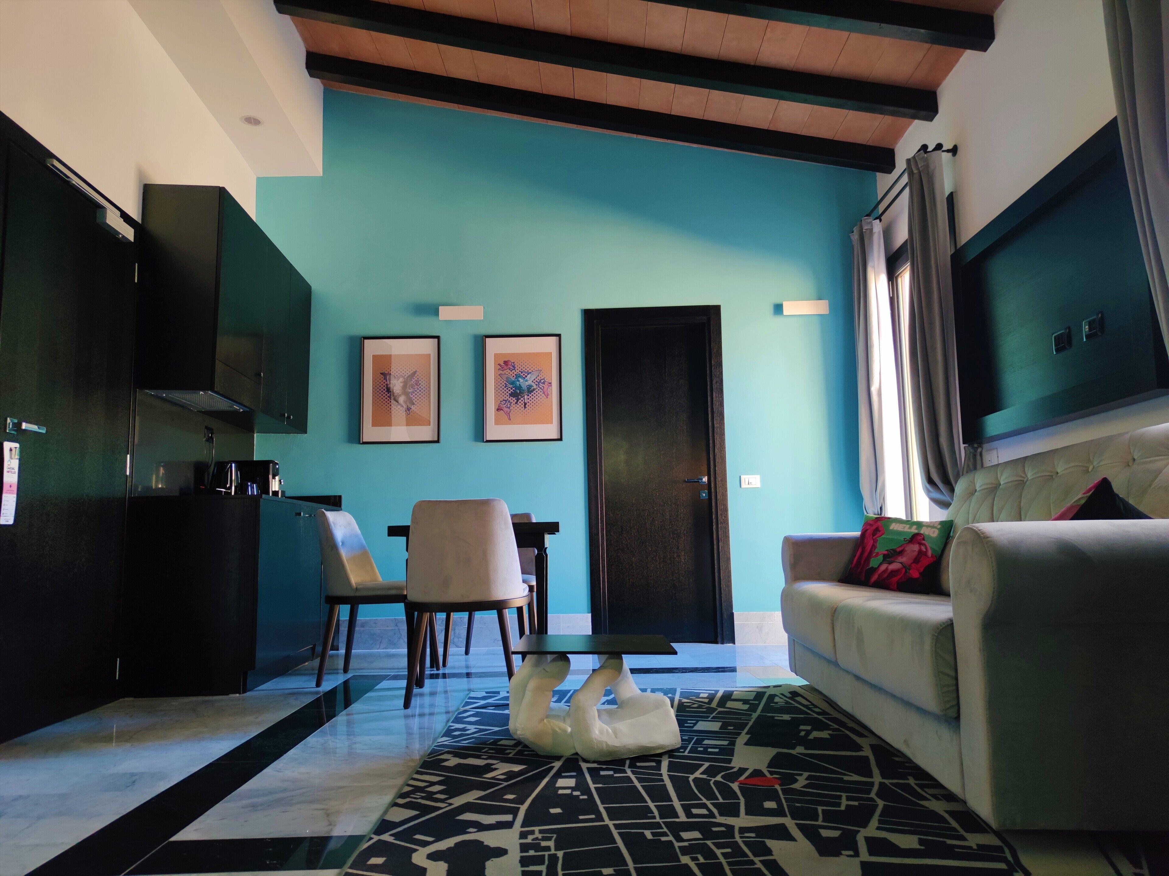 Una sala moderna con una pared de acento color turquesa, un sofá, una mesa de centro y un comedor con sillas.