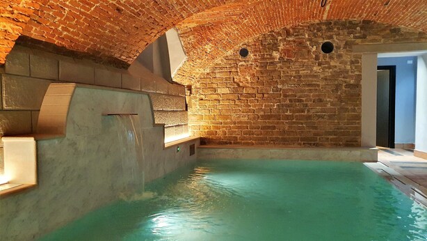Une piscine intérieure avec un mur en briques et un bord en béton.