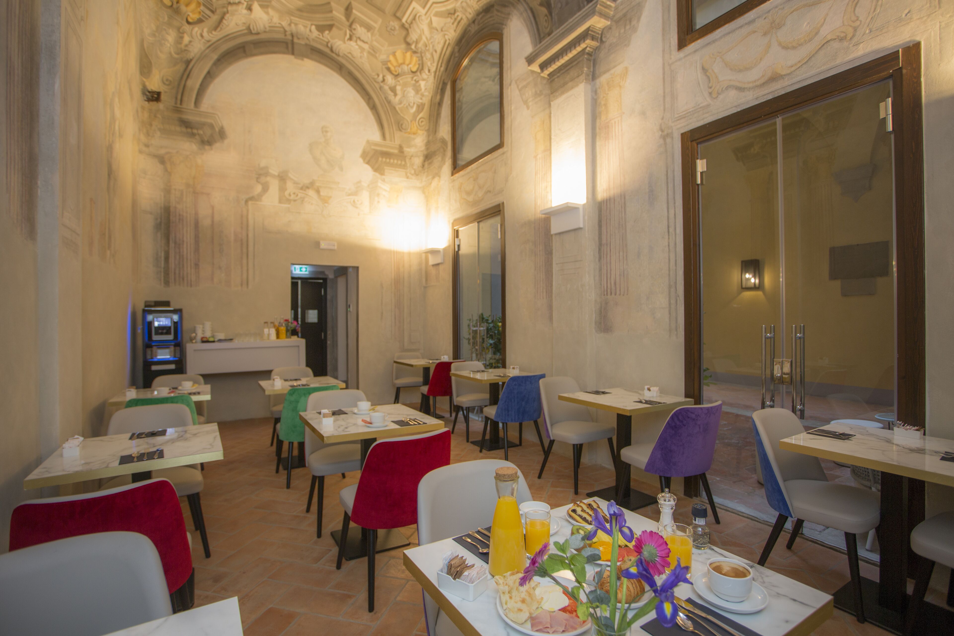 Un restaurant avec des tables en marbre, des chaises rouges et grises, et une variété de plats pour le petit-déjeuner disposés sur les tables.
