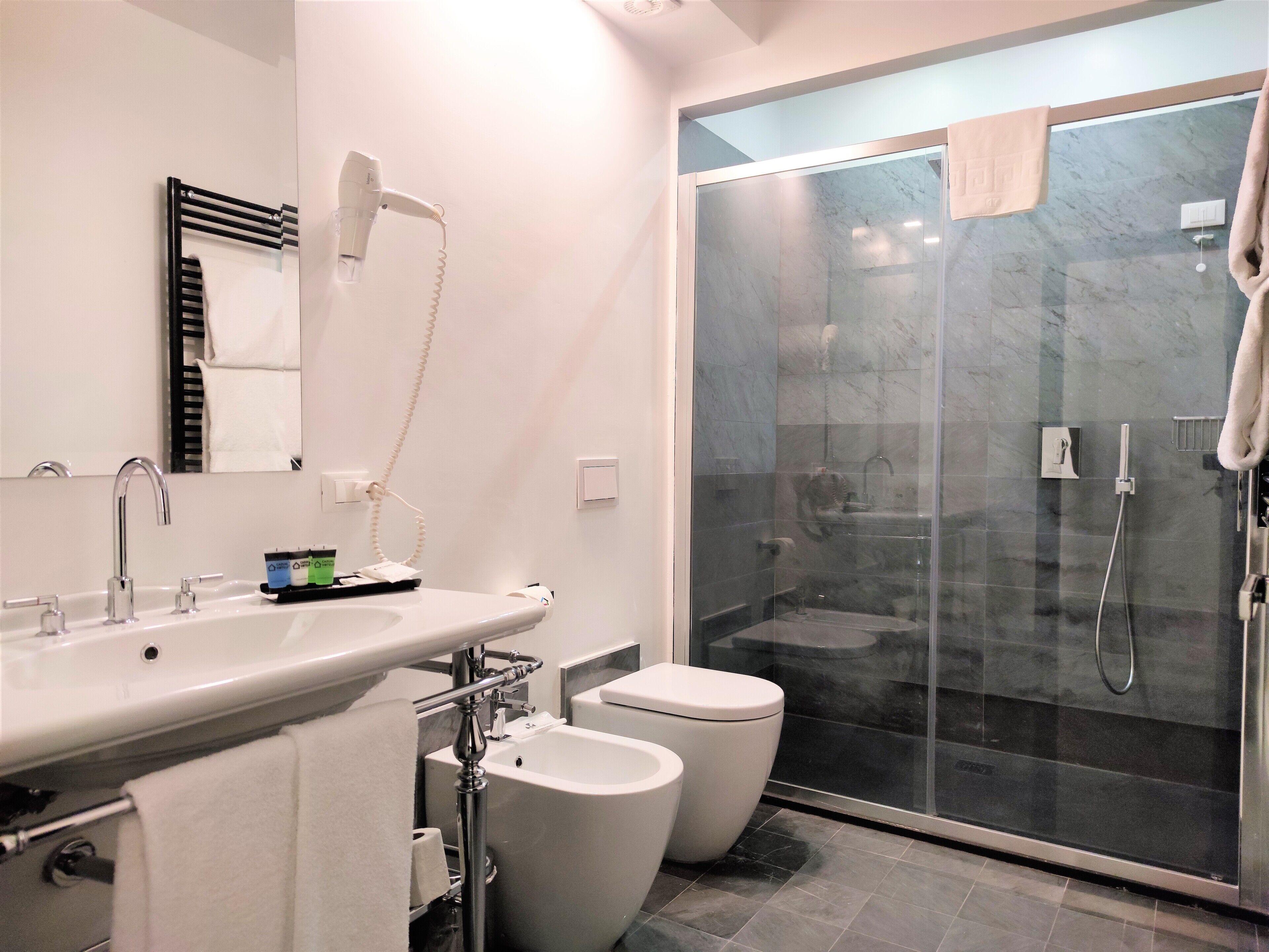 Een moderne badkamer met een douchecabine van glas, een witte wastafel met spiegel en twee toiletten.