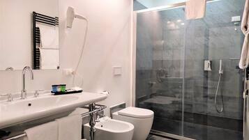 Een moderne badkamer met een douchecabine van glas, een witte wastafel met spiegel en twee toiletten.