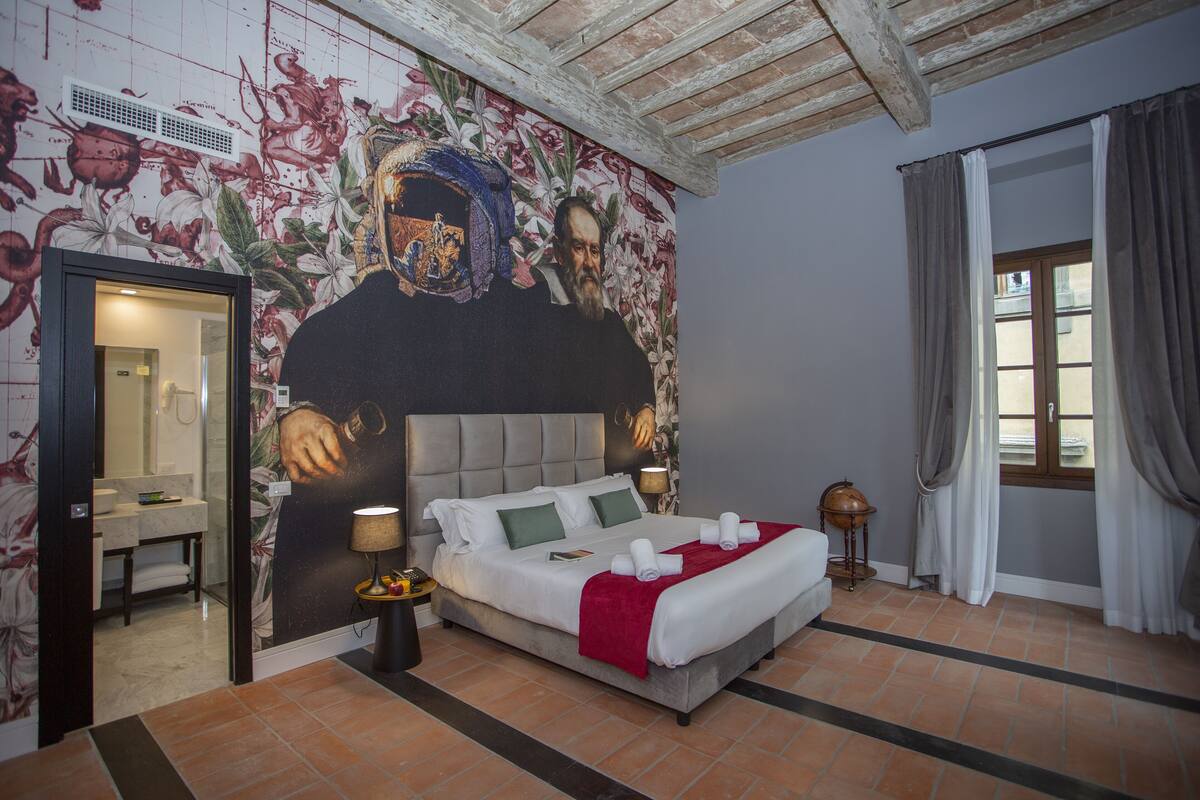 Un dormitorio con una cama grande, un baño visible a través de una puerta abierta y un mural en la pared.