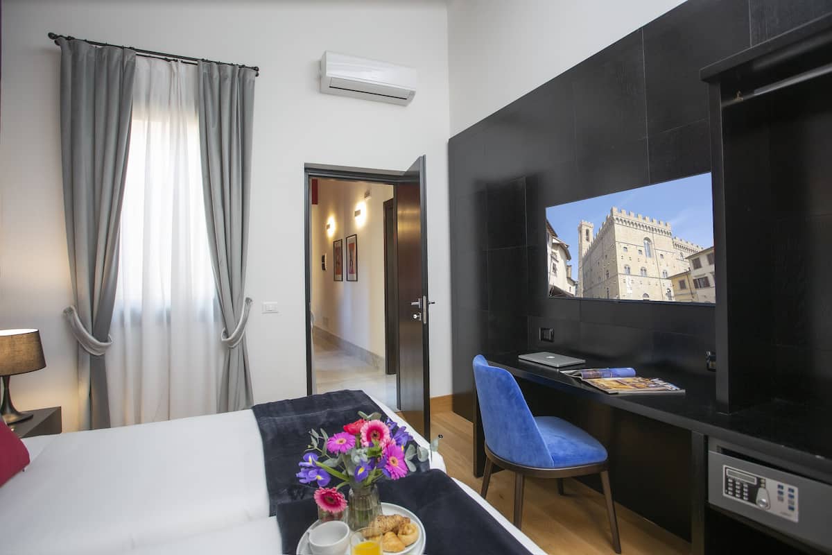 Una habitación de hotel con cama, una mesa de comedor con una silla, un televisor y una ventana con cortinas.