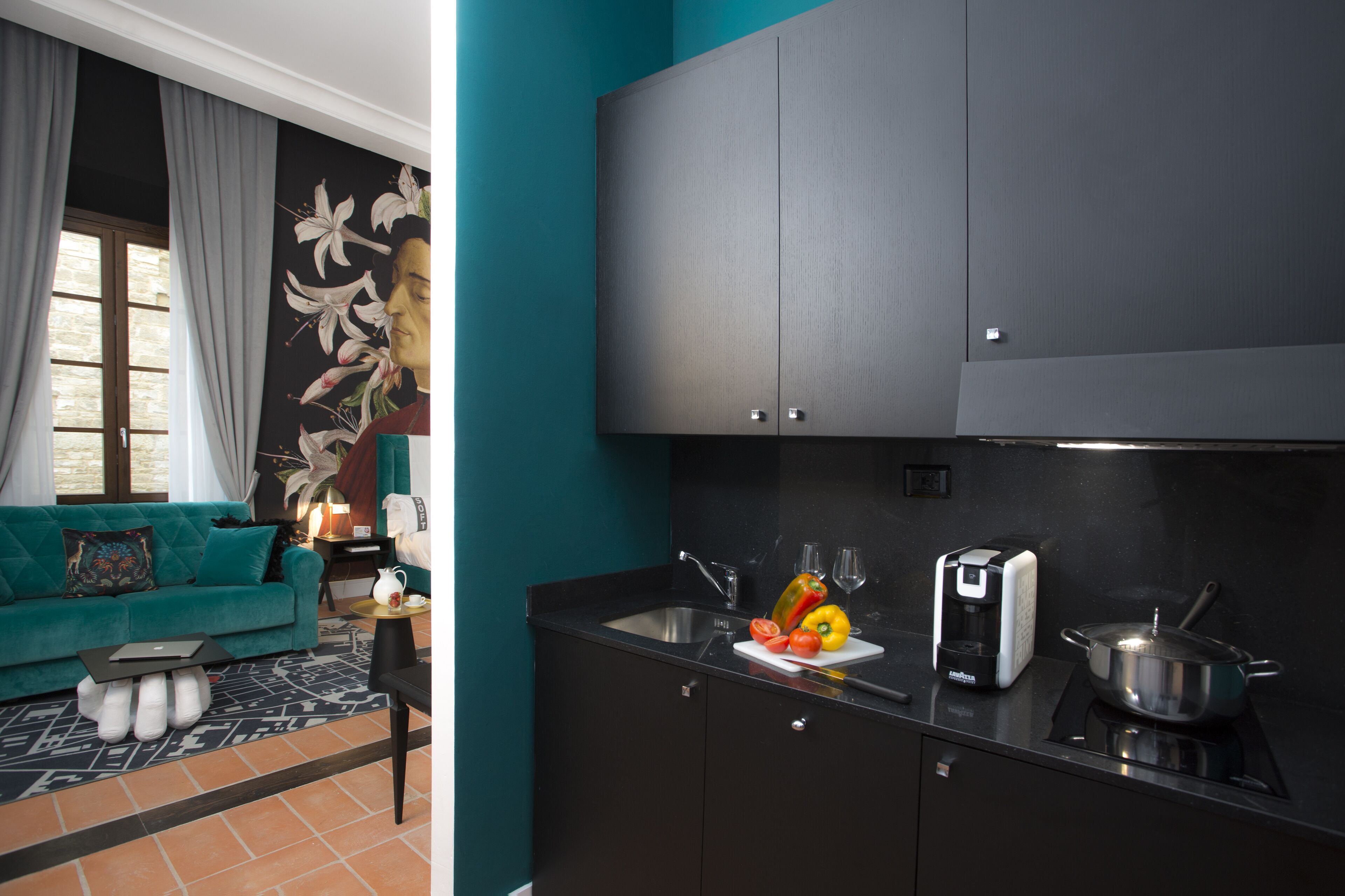 A modern kitchen with a black countertop, a sink, and a stove. There is a teal sofa with a patterned throw pillow in the adjacent living area.