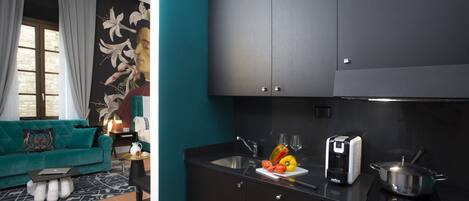 A modern kitchen with a black countertop, a sink, and a stove. There is a teal sofa with a patterned throw pillow in the adjacent living area.